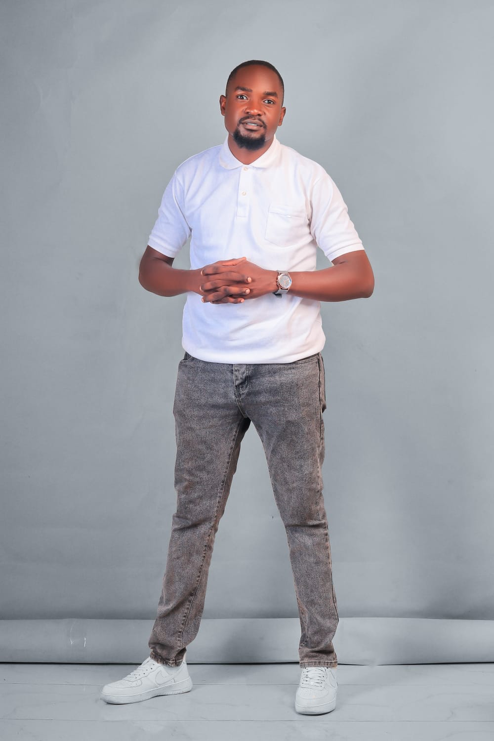 Dismus Nganyi standing in a white polo shirt and grey jeans against a studio backdrop